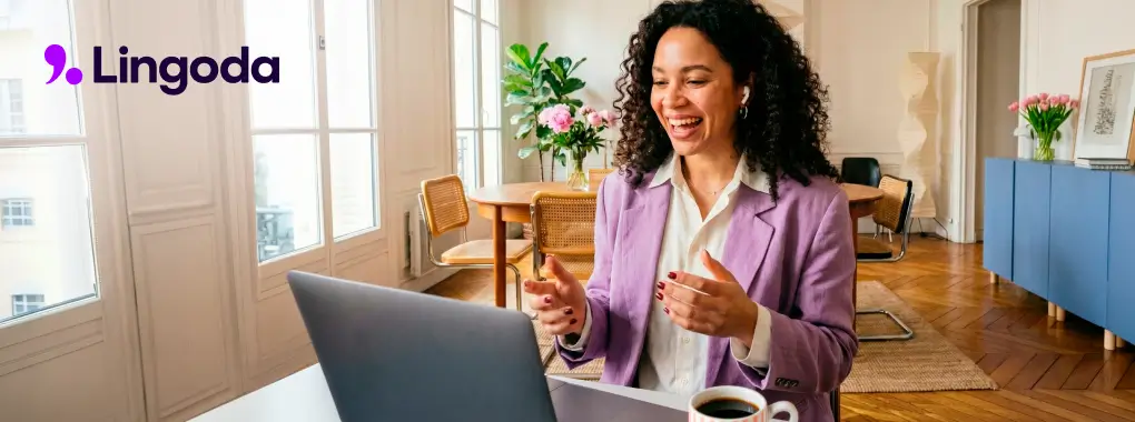 screenshot of a smiling woman sat infront of an open laptop during a Lingoda language learning session, logo in the top left corner
